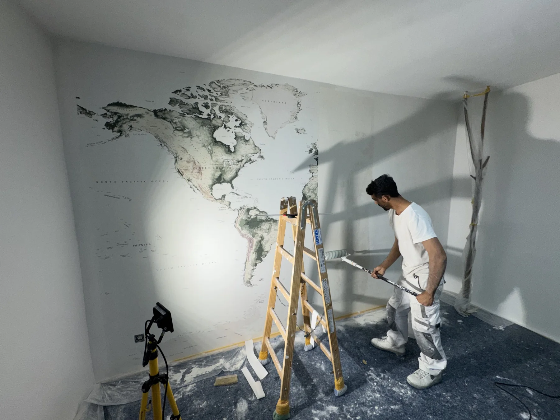 Dekoral-Mitarbeiter beim Streichen einer Wand neben einer dekorativen Weltkarten-Tapete