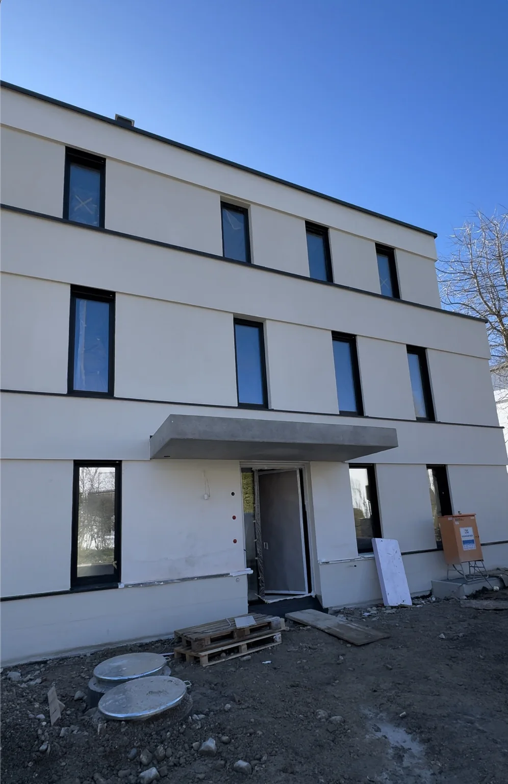 Helle Fassade eines mehrgeschossigen Hauses mit dunklen Fensterrahmen während der Bauphase